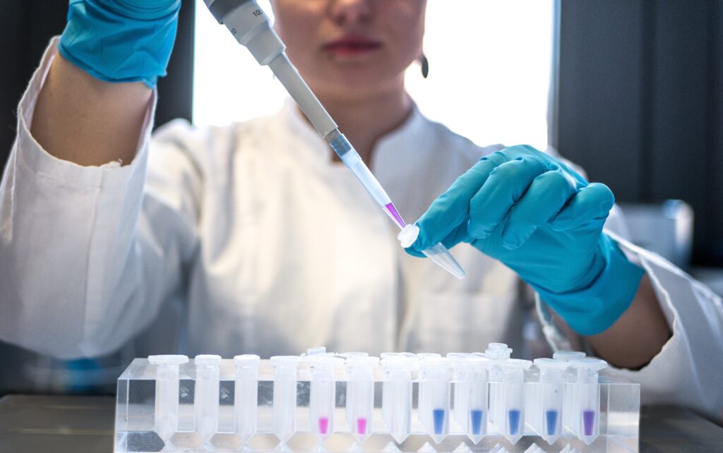 Técnico con guantes azules pipeteando muestras líquidas en tubos de ensayo de laboratorio