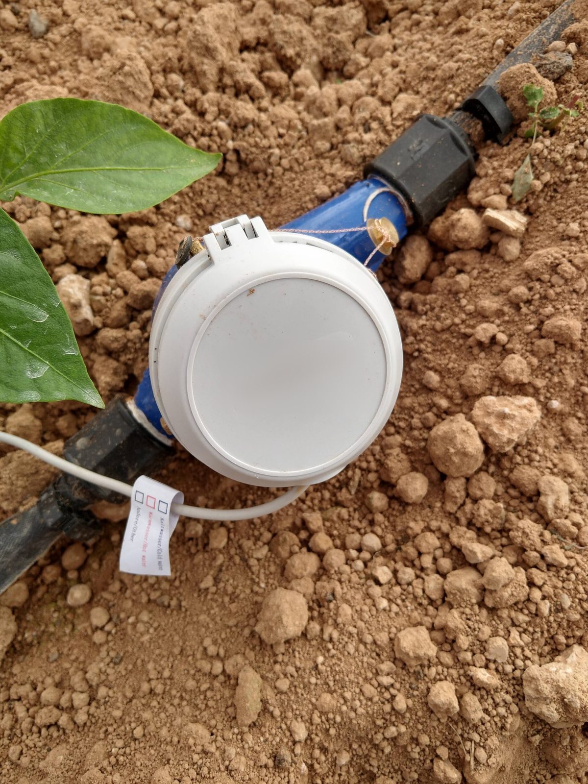 Contador de agua de riego con emisor de pulsos acoplado, junto a la tubería en campo