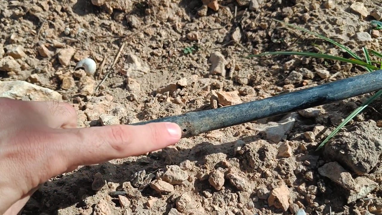 Mano señalando la tubería de goteo sobre un suelo seco y pedregoso, donde se elige el punto de medición